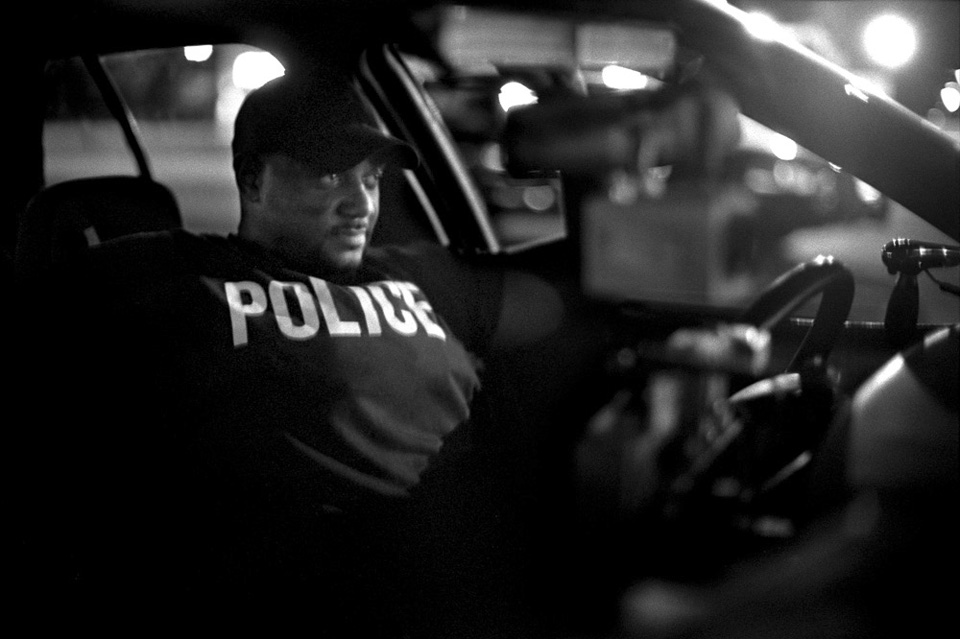 A wary Detroit police officer watches a crowd after an arrest on the East Side.