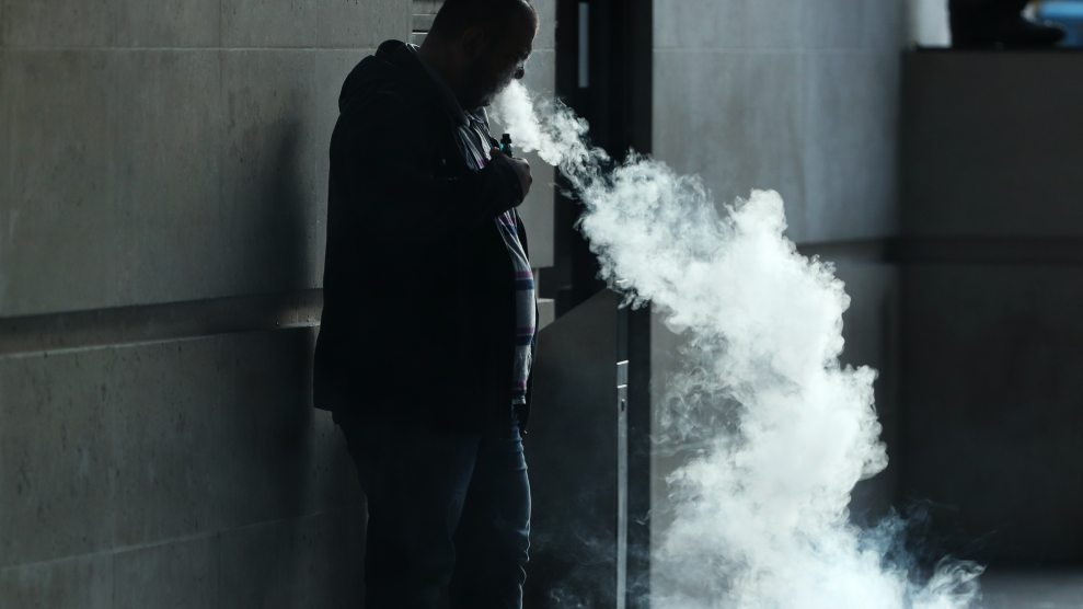 A bald man in shadow leans against a stone wall, exhaling a huge cloud of vapor.