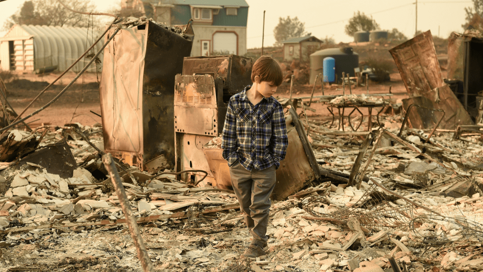 A young boy surveys the brown wreckage of a home
