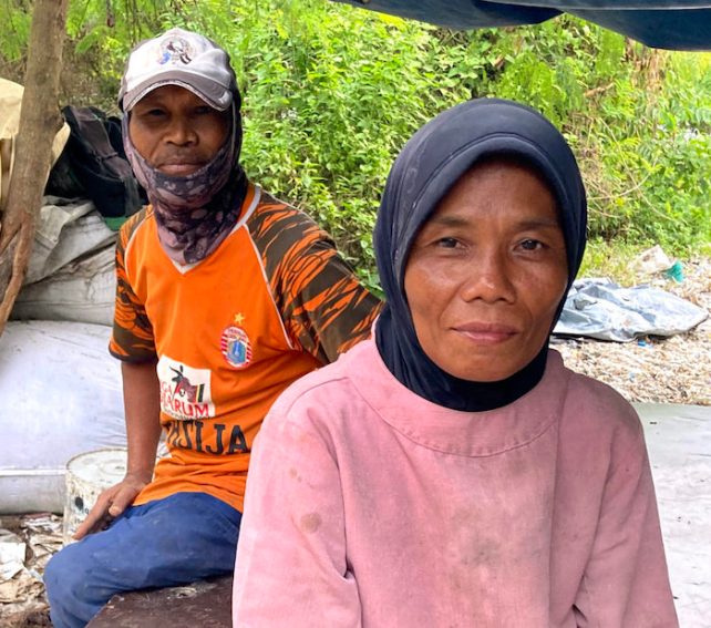 Kasih, who has brown skin and is wearing a black head covering and pink top, next to her husband, wiho has dark brown skin, wearing a cap, orange shirt and jeans. 