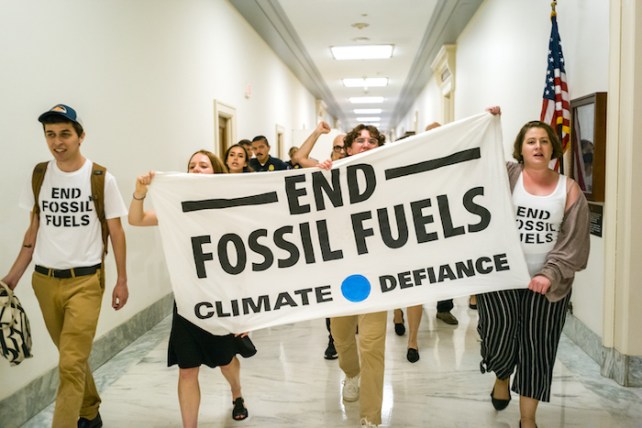 Young protestors holding up a sign that says "End Fossil Fuels: Climate Defiance," with some wearing shirts that say "Climate Defiance" on them