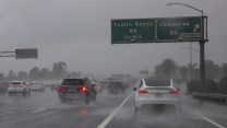 Cars slow on a rainy highway. A sign reads "Tustin Ranch Rd" and "Jamboree Rd."