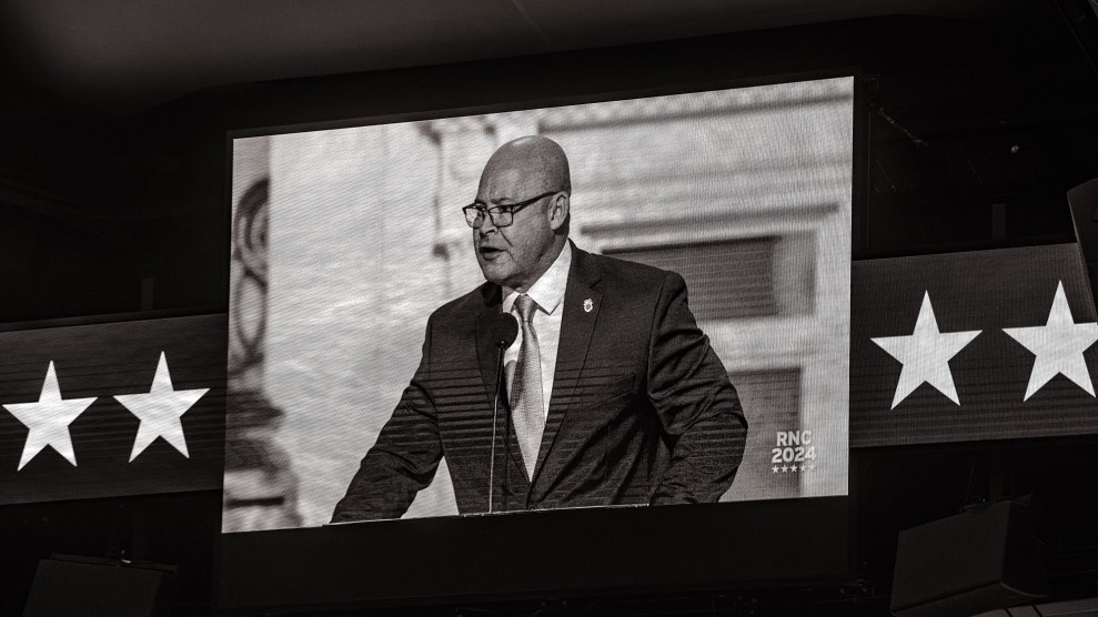 Black and white photo of a bald man speaking, as shown on a screen with stars on both sides.