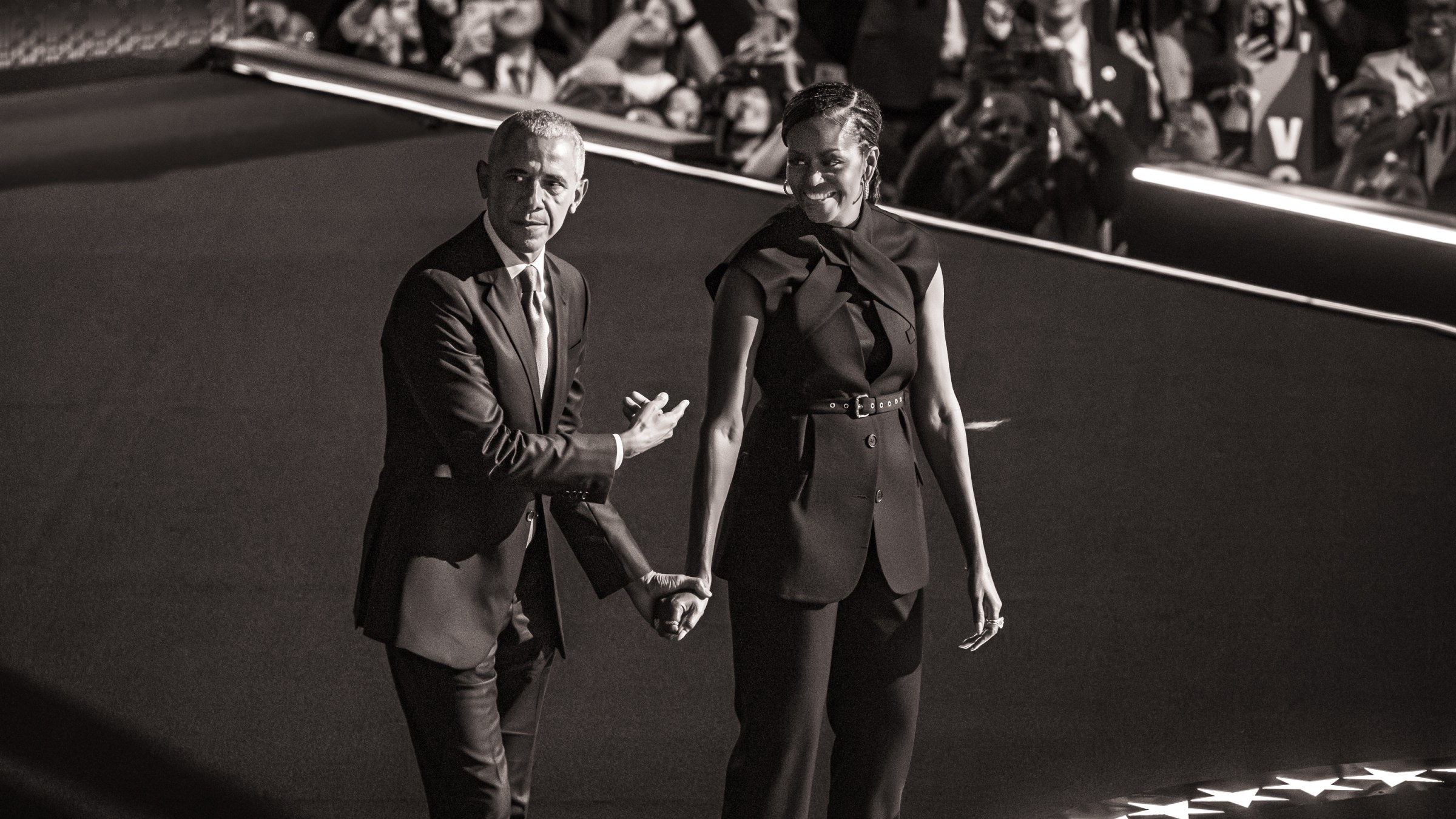 Black and white photo of Barack Obama holding hands with and pointing at Michelle Obama.