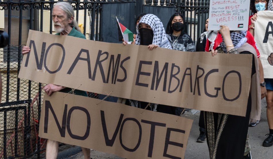 People hold a sign reading "no arms embargo, no vote"