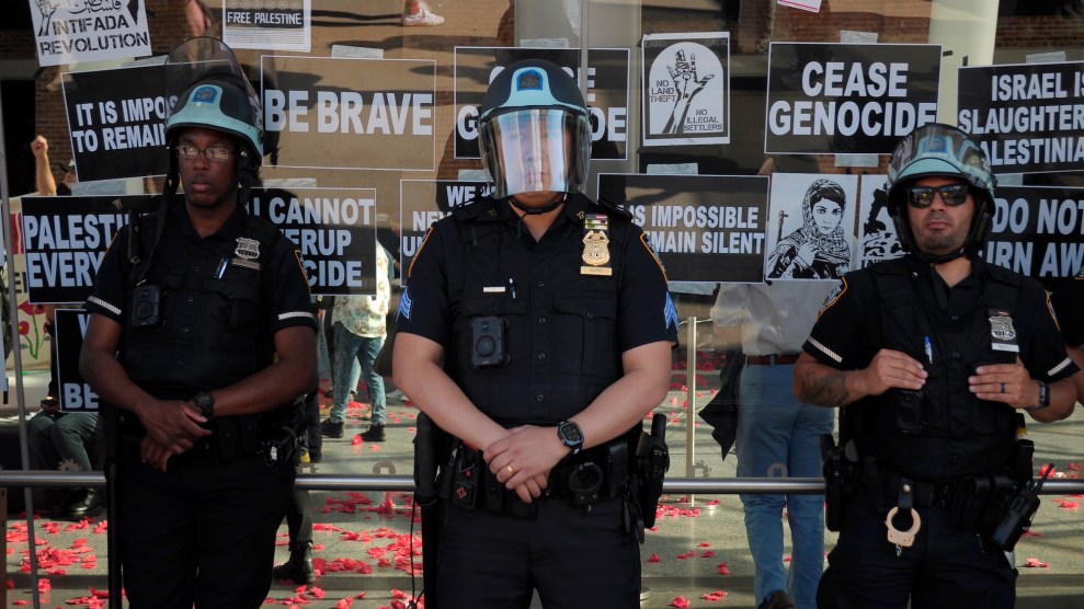 Three police officers in front of a glass building with signs on it including "Cease Genocide," "Israel is slaughtering Palestinians" and "Intifida Revolution"