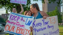 A mother kisses her daughter's head as both hold signs in support of abortion rights