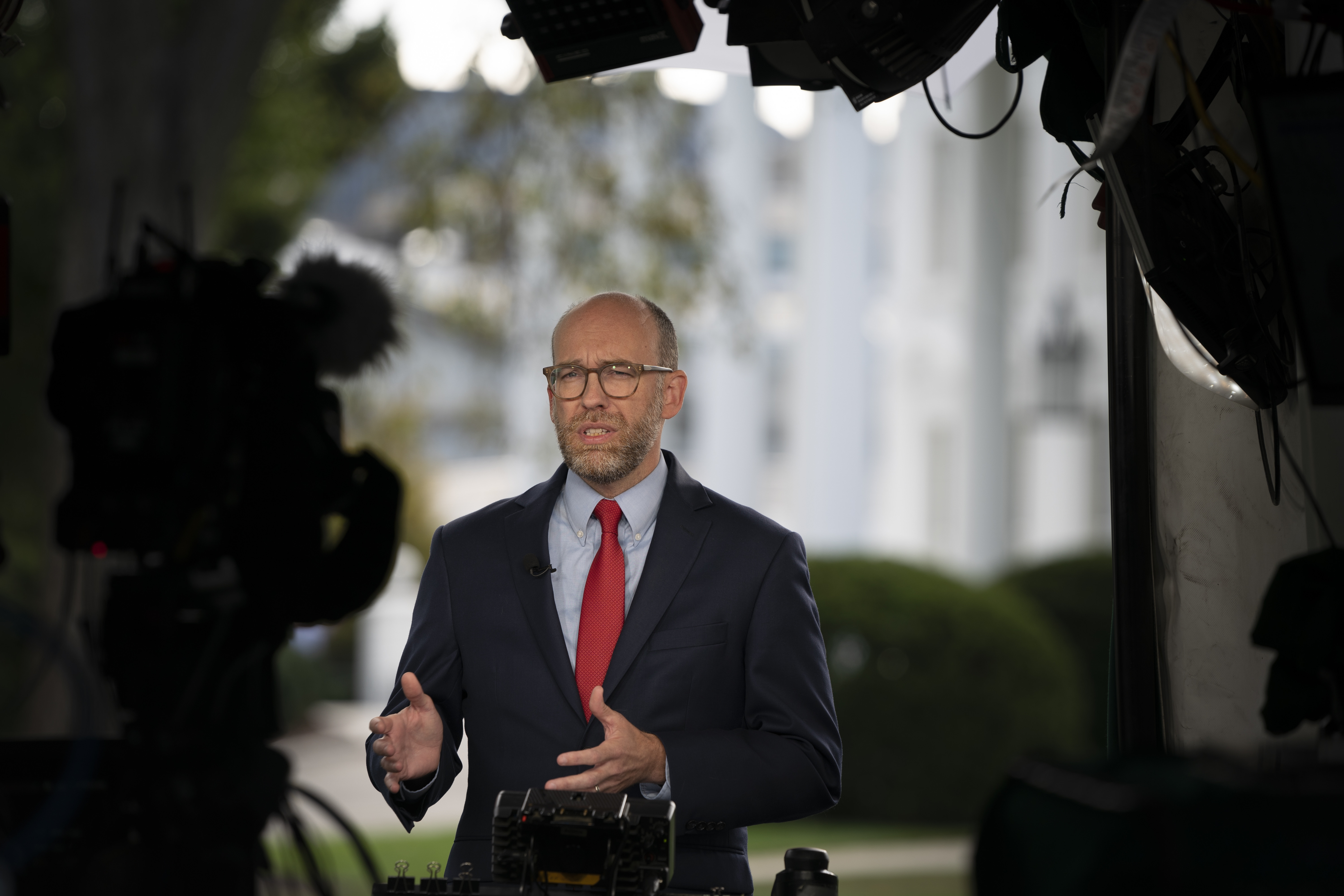 Russell Vought stands with hands outstretched in front of camera and lights on the White House lawn.