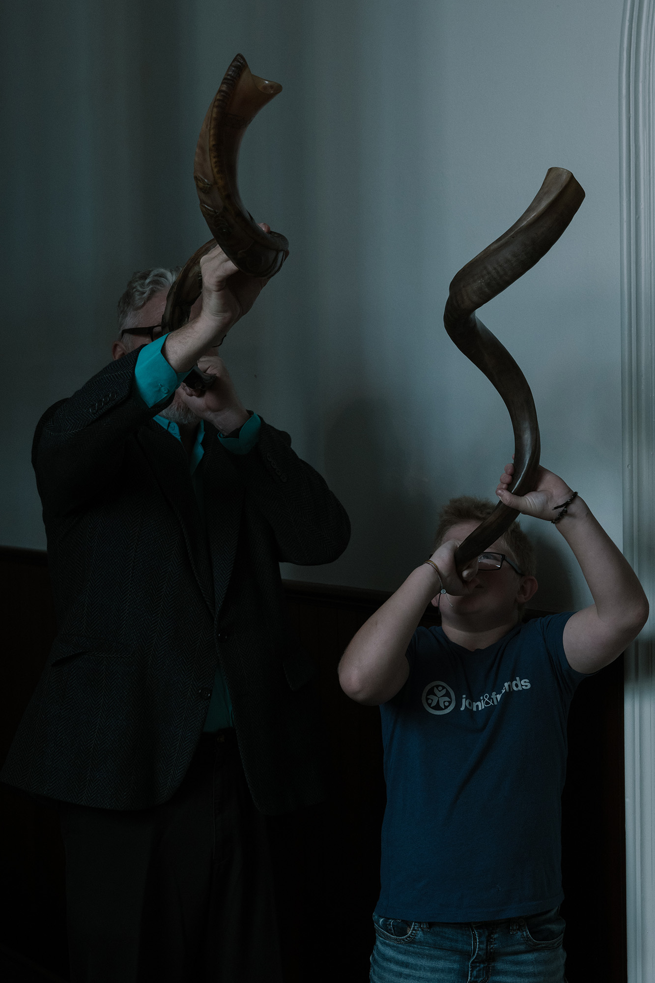 A father and son raise and blow through curved horns.