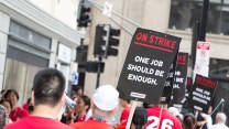 Workers in red shirts hold up black picket signs.