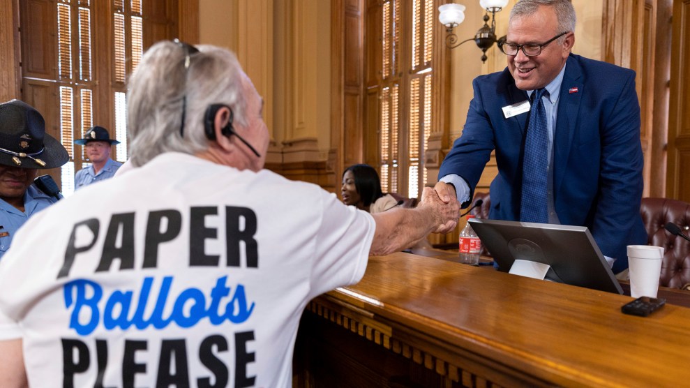 Man wearing a shirt that reads, "Paper Ballots Please," shakes the hand of another man in a suit and tie.