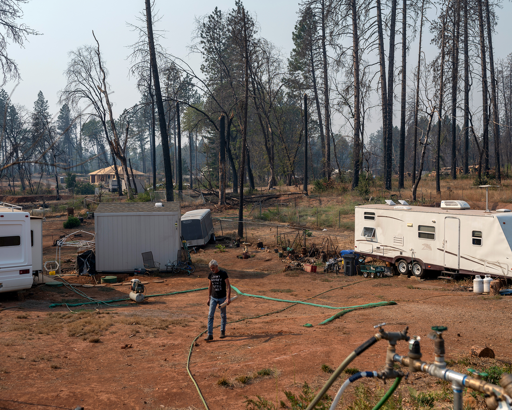 Man walks in an area burned by wildfires. Two RVs are nearby.