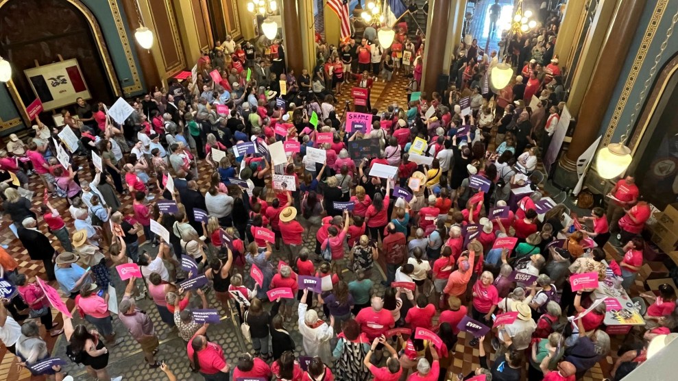 Many in a gathered crowd carrying signs and are wearing bright pink shirts.