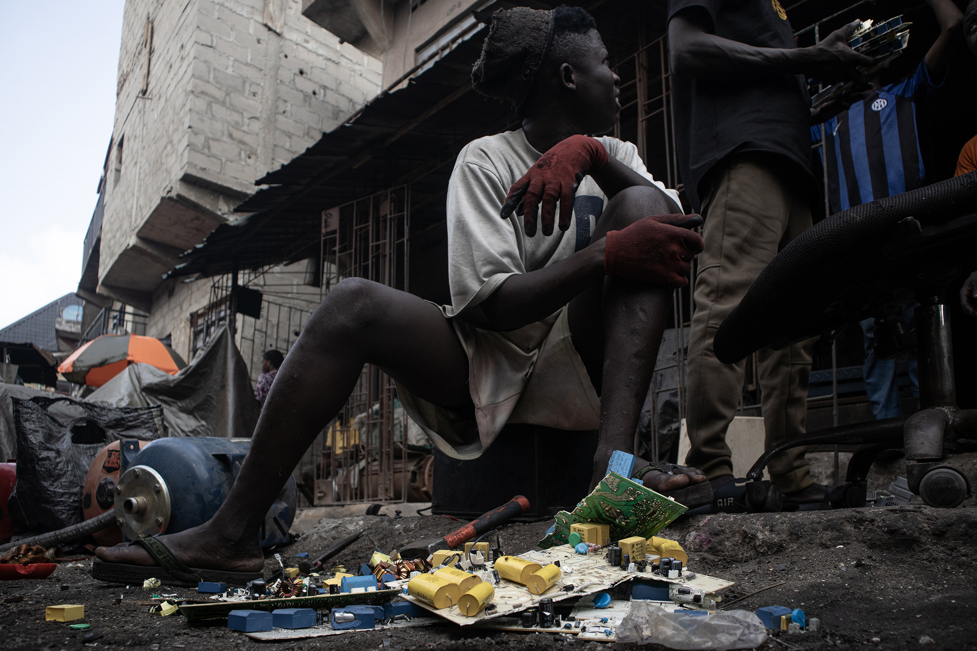 Boy sitting on a sidewalk with computer parts in front of him. 