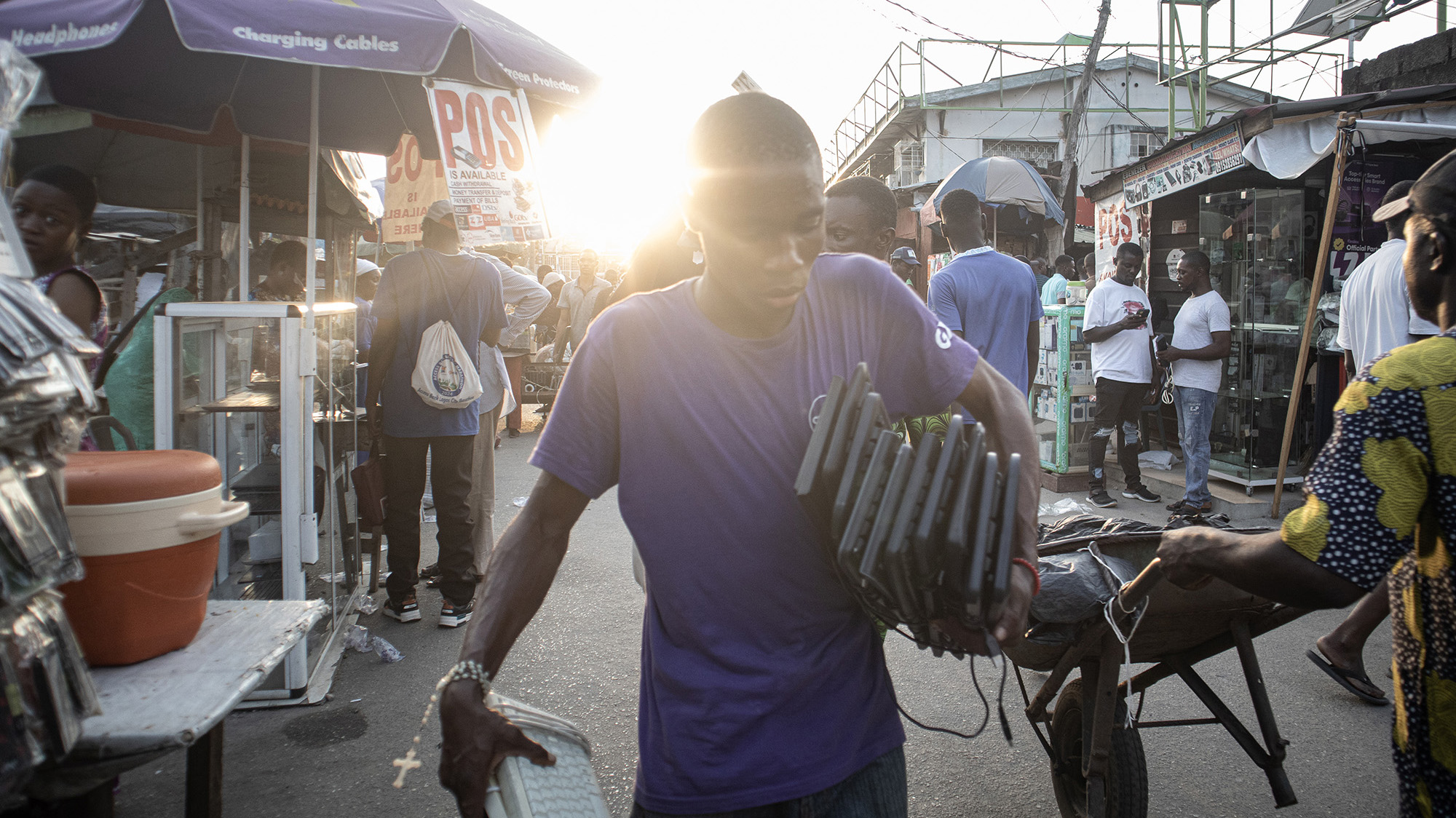 Young black man in blue shirt carrying computer keyboards under his arm in a market.