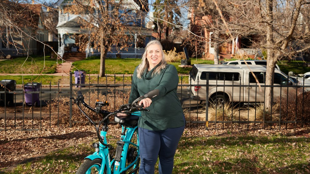 Luchia holds her blue electric bike in her lawn on a fall day.