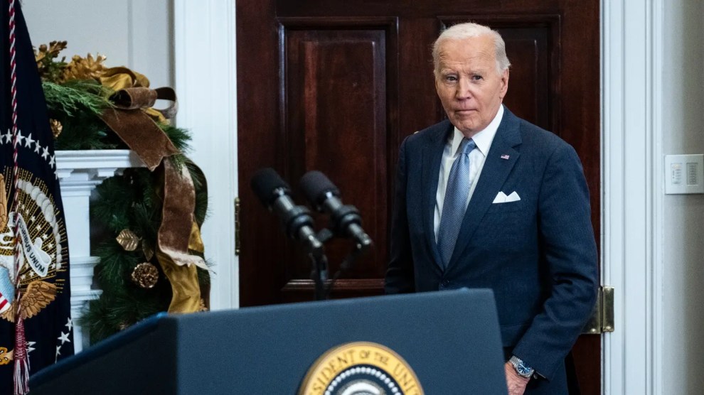 A white man walks to a podium wearing a suite and blue tie