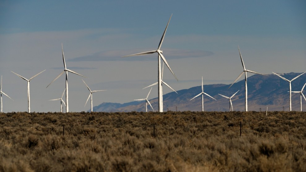 A handful of windmills spin in a cast field with mountains rising in the background.