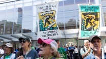 Climate activists wearing baseball caps hold signs saying "Stop the Money Pipeline to Climate Destruction."