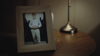 A still image from a documentary depicting a picture frame of an older gentleman (Pedro Moreno) standing in front of a backdrop of a night city.