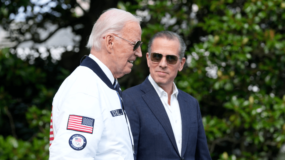 Hunter Biden wearing a suit looks at Joe Biden wearing a team USA jacker with a slight grin.