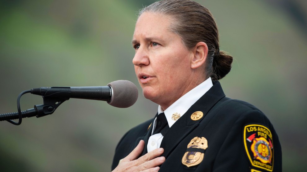 A white woman wearing a LA fire department dress uniform, with brown hair pulled back tightly into a bun, speaks into a microphone