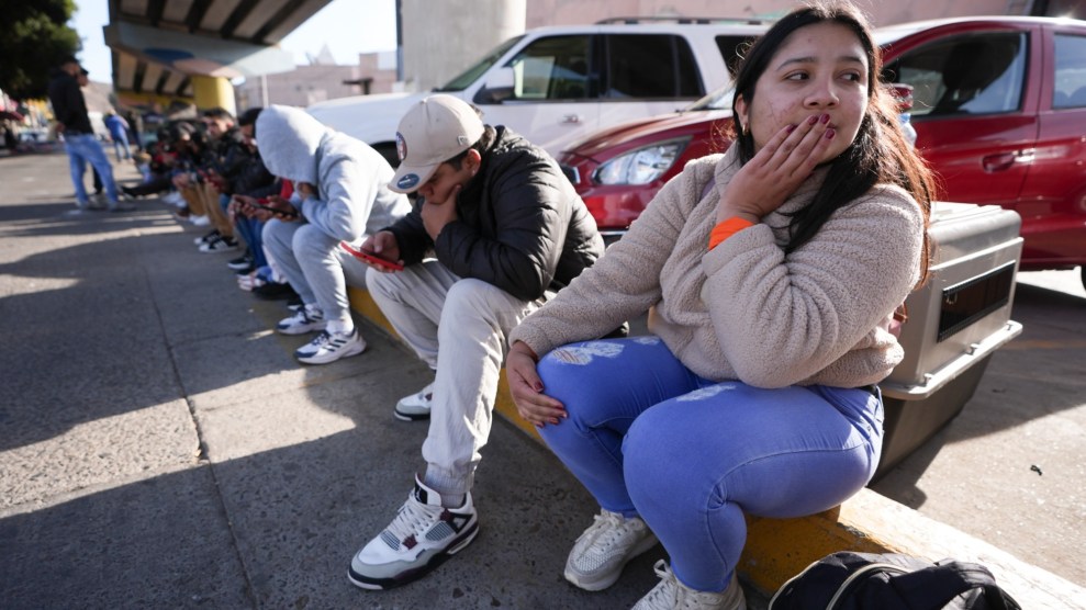 People sit in a line along the curb of a parking lot.