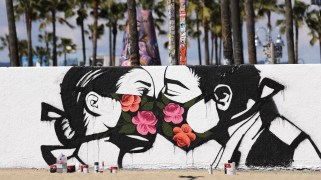 A mural at a beach of two people kissing while wearing floral masks.