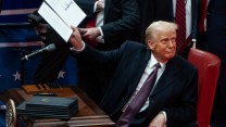 A white man wearing a suit and tie holds up a signed paper.