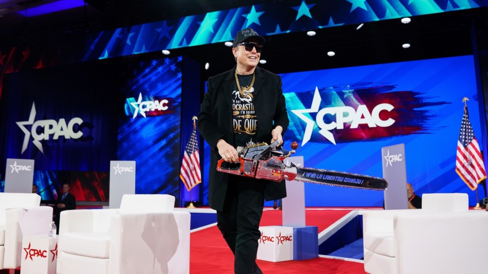 Elon Musk on a stage with CPAC logos behind him, wearing sunglasses and a black baseball cap and holding a chainsaw.