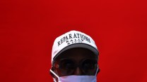 A person in a white baseball cap reading Reparations Rally in front of a red backdrop.