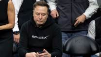 Elon Musk, in black SpaceX sweatshirt, looking at his phone.
