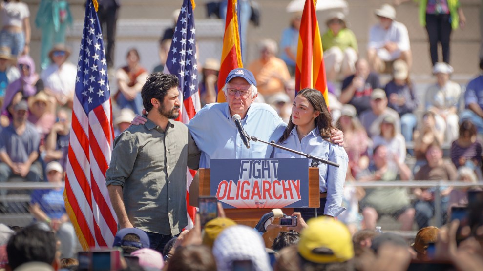 Bernie Sanders stands on a podium with a sign that reads "Fight Oligarchy," with his arms around Greg Casar and Alexandria Ocasio-Cortez.