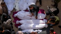 People crowded around dead bodies wrapped in white sheets.