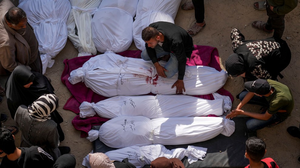 People crowded around dead bodies wrapped in white sheets.