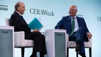 Two white men sit on white chairs in front of a blue wall that says CERAWeek.