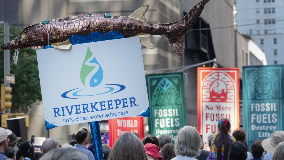 A poster that says "Riverkeeper NY's Clean River Advocate" with a sculpted fish on top. With its handmade fish sculpture, Riverkeeper's sign stands out at the March to End Fossil Fuels, New York, New York. Several tall banners denouncing fossil fuels are visible in the background. Riverkeeper is an environmental organization focusing on protecting the Hudson River and advocating on clean drinking water issues.