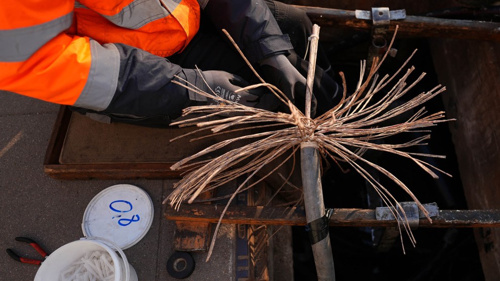 Copper wires splay from a cord in every direction. Arms wearing bright orange reach from off-shot to fix them.