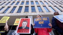 Protesters hold signs that read 'fund education not 1% tax cuts,' 'I am stealing from you' with a drawing of Elon Musk, and 'Remove DOGE now.'