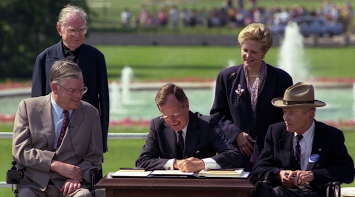 George H. W. Bush signing a piece of paper outside, surrounded by four people