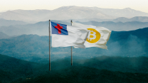 Two flags billow in the wind as they fly above the Appalachian mountains. The one on the left is the Christian Flag, which has a white field, with a red Latin cross inside a blue canton. To the right, partially obscured by the Christian Flag, is another white flag, but this one has a gold circle at the center. Inside the gold circle is the iconic, slightly tilted Bitcoin logo, which is a stylized capital letter “B” with two vertical strokes through it, similar to a dollar sign.