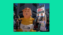 A horizontal photo of protestors on a bright green background. In the photo, a woman in a pink shirt and sunglasses holds a sign that reads "HANDS OFF! CREEPY LOSER.' To the left of the protestor is an inflatable balloon of Donald Trump charactered as a baby. The baby is shirtless, but wears a diaper. Trump, as the baby, appears to be crying.