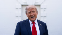 Donald Trump speaking in a blue suit and red tie against a white background.