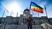 A person walks up state capitol stairs with a rainbow flag.