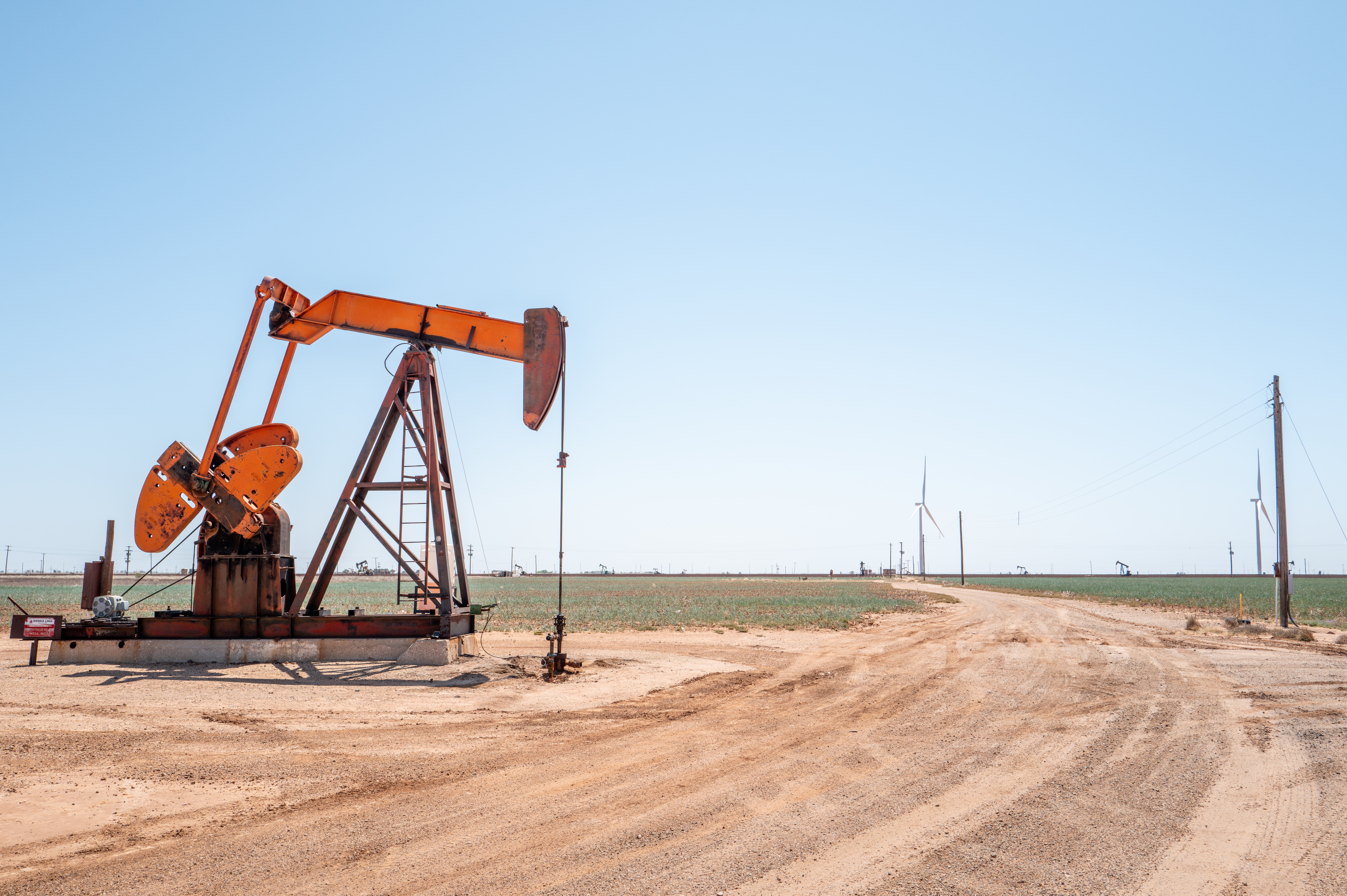 A red oil pumpjack next to a dusty road and a blue sky.