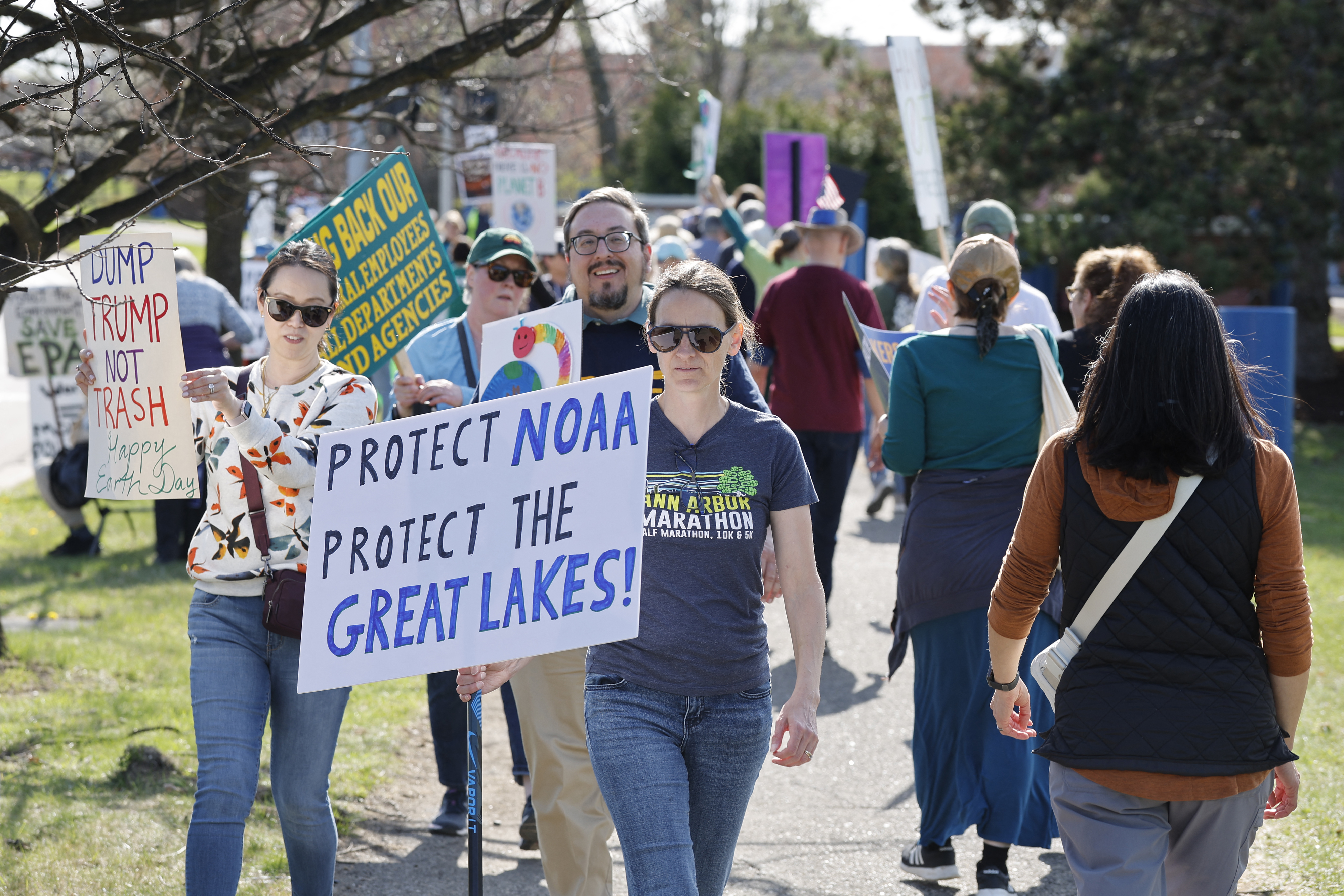 A person holds a sign that says "Protect NOAA Protect the Great Lakes" They are surrounded by many others with obscured signs.