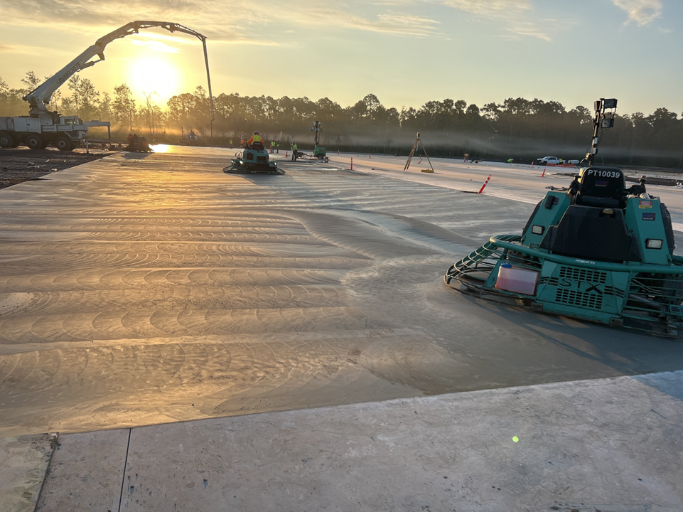 A green machine flattens fresh concrete while the sun sets
