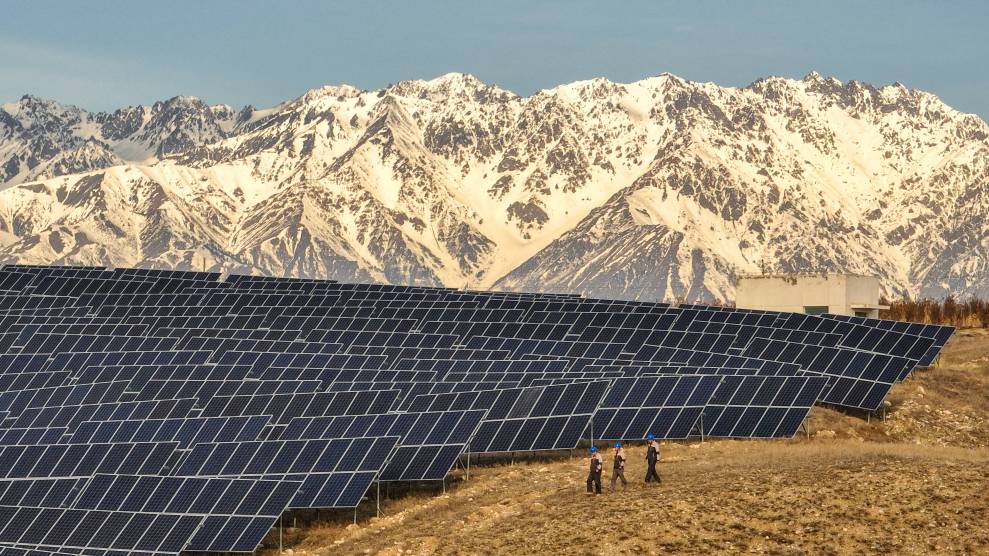 A large solar array on a barren hill in front of snowy mountains.