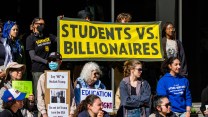 In a group of protesters, several people hold a large black-and-yellow banner that reads, “Students vs. Billionaires.”