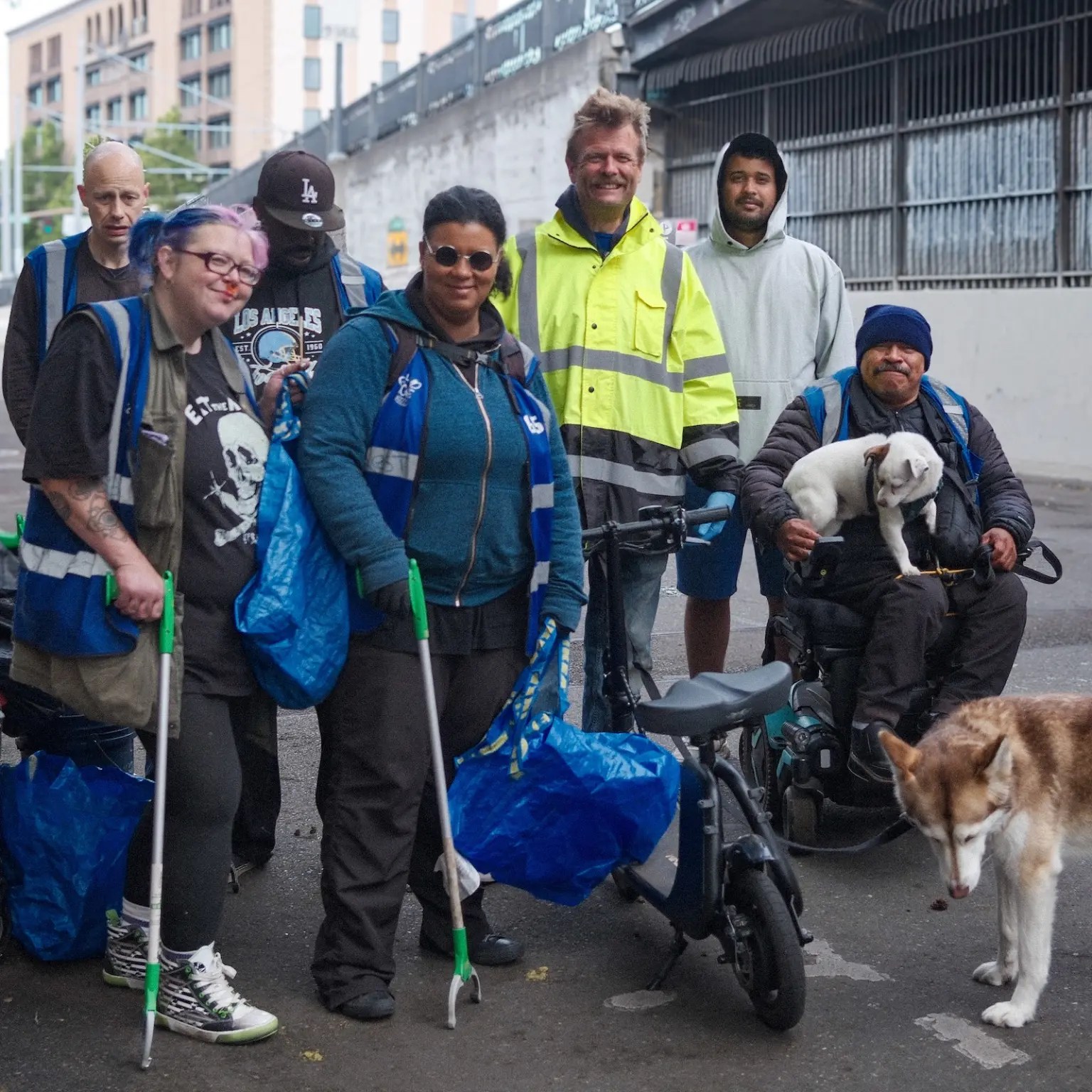 Seven people and two dogs pose together smiling with bags to pick up bottles and cans.